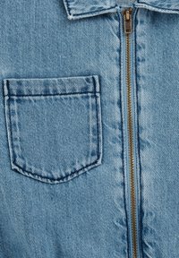 Lichtblauwe denimjack met een voorkant met ritssluiting en gouden hardware, een klein borstzakje en een soepele textuur.