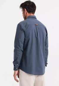 Herren Langarmhemd aus navyblauem Stoff mit einer Knopfleiste an den Manschetten, Rückenpasse und einem kleinen Lederetikett am Kragen. Glatte Textur.
