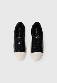 Une paire de baskets noires Armani Exchange avec des embouts et des semelles blanches, des lacets noirs et un logo sur la languette et les côtés.