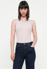 Top fără mâneci de culoare roz deschis, cu un design ajustat, asortat cu blugi din denim de culoare albastru închis, cu talie înaltă, dotati cu buzunare frontale și închidere cu nasture.