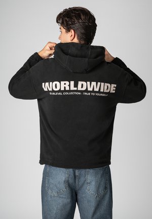 Schwarzer Fleece-Hoodie mit großem weißem Schriftzug "WORLDWIDE" auf der Rückseite, darunter der Text "SUBLEVEL COLLECTION - TRUE TO YOURSELF".