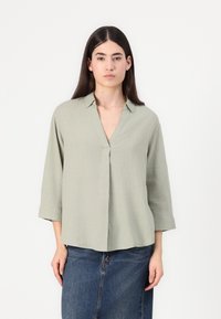Ljusgrön blus med v-ringning, uppvikt ärm och lös passform. Tillverkad i ett texturerat material, har den en mittveck och minimalistisk design.