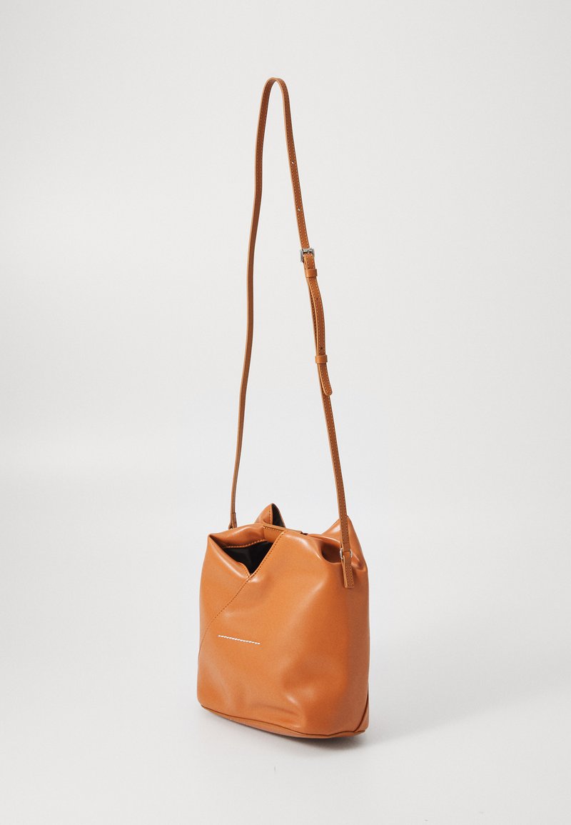 Piccola borsa a secchiello in pelle beige con lunga tracolla regolabile su sfondo chiaro uniforme.