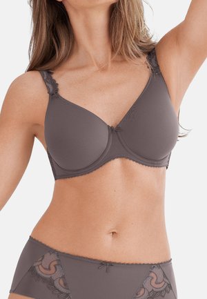 Frau trägt passenden grauen BH und Slip mit Spitzendetails, posiert mit einem erhobenen Arm vor einem schlichten weißen Hintergrund.