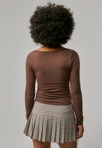 Brown long-sleeve top with a fitted design, paired with a pleated, short plaid skirt featuring a zip detail and checkered pattern.