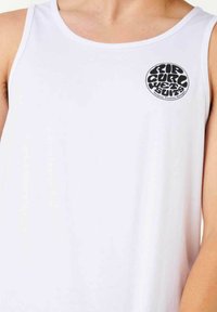 Weißes ärmelloses Tanktop mit einem runden schwarzen Logo im linken Brustbereich. Das Material wirkt glatt und leicht mit einem klaren Design.