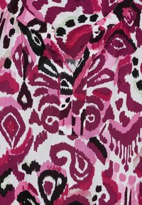 Kortärmad blus med ett abstrakt floral mönster i rosa, svart och vitt, med en urklippt hals och rynkad tyg runt halslinningen.