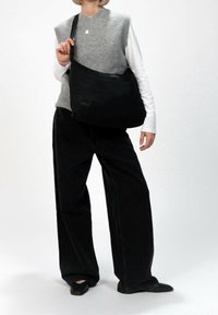 Černá nylonová taška přes rameno s nastavitelným popruhem, hladkou texturou, minimalistickým designem a zapínáním na zip, nesená osobou v neformálním oblečení.