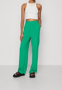 Zelené široké kalhoty z lehké látky, s vysokým pasem, dvěma bočními kapsami a hladkým povrchem. V kombinaci s bílým crop topem.
