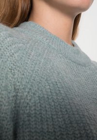 Maglione lavorato a maglia azzurro chiaro con scollatura rotonda, caratterizzato da un tessuto testurizzato e da dettagli a coste sul colletto. Design morbido e informale.