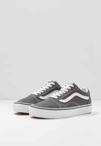 Szare zamszowe sneakersy z białymi akcentami, z klasycznym designem na sznurówki i białą gumową podeszwą. Wyraźny czarny obramowanie wokół podstawy.