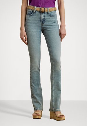 Jeans en denim bleu clair avec une coupe slim, dotés d'une ceinture tissée beige et de poches avant. Portés avec des sandales compensées beiges.
