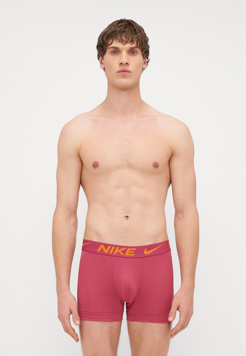 Crvene Nike bokserice s žutim logoom branda na pojasu. Materijal je gladak, s uskim fitom i minimalnim šavovima.