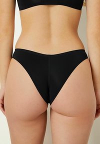 Slip bikini neri con design a vita bassa, caratterizzati da una texture liscia e aperture laterali alte. Adatti a una varietà di tipi di corpo.