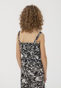 Top in stampa floreale bianco e nero con spalline regolabili, texture arricciata e orlo a frange, che mette in mostra una silhouette aderente.