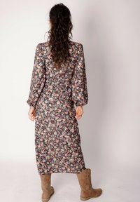 Sukienka maxi w kwiaty z długimi rękawami, czarne tło, wielokolorowe kwiaty, talia podkreślona, zestawiona z beżowymi kozakami za kolano.