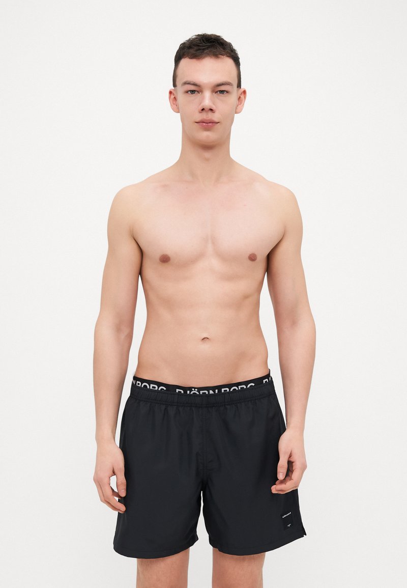 Calções de banho pretos com um cós elástico, apresentando um logótipo da marca em contraste. Feitos de material leve e resistente à água.