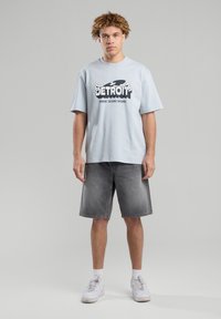 Sky blue cotton short-sleeve T-shirt with black graphic print "DETROIT WHERE TECHNO BEGINS". Worn with faded gray denim shorts and white sneakers.