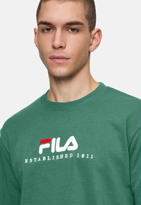 Groene katoenen sweatshirt met een ronde hals en geborduurd FILA-logo met rode en witte accenten, tekst luidt "OPGERICHT 1911."