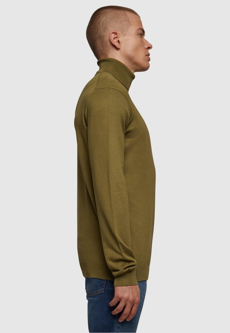 Olivgrön polotröja i mjukt, strukturerat tyg; åtsittande design med ribbad mudd och nederkant; kombinerad med blå jeans; sidovy.