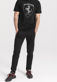 Camiseta negra de algodón con un logo gris de Ferrari, combinada con pantalones sudadera negros y zapatillas negras con acentos rojos.