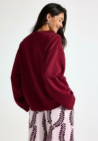 Bordeaux sweatshirt med dropped shoulders og ribbestrikket kant, parret med en lyserød nederdel med et mørkt bladmønster.