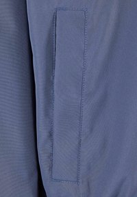 Gros plan d'une poche en tissu bleu avec des coutures visibles sur un vêtement, montrant la texture et les détails des coutures.