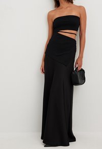 Černý dvoudílný outfit obsahující top bez ramínek s výřezem a asymetrickou sukni. Vyrobeno z hladké látky s volným designem.