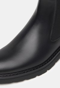 Stivaletto in pelle nera con una finitura liscia, pannello elastico laterale, punta arrotondata e suola in gomma texturizzata.