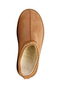 Chausson en daim beige avec un bout arrondi, une doublure intérieure moelleuse, des coutures blanches le long du bord et une petite languette à l'arrière.