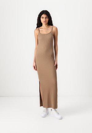 Brown ribbed knit maxi dress with thin straps and a side slit, paired with white sneakers, featuring a fitted silhouette.
