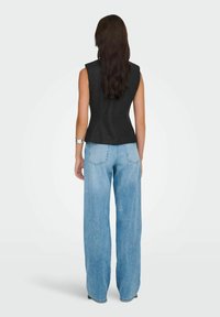 Top nero senza maniche con design aderente, abbinato a jeans a gamba larga blu chiaro. Tessuto con texture liscia, dettagli minimi, silhouette dritta.