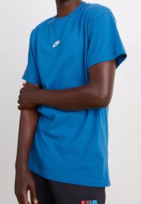 Modrá bavlněná tričko s kulatým výstřihem a krátkým rukávem, s malým bílým logem Nike na hrudi. Hladká textura, standardní střih.