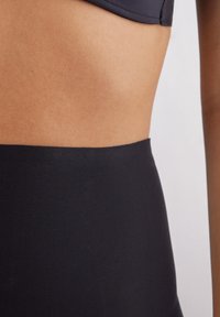 Černé plavkové kalhotky s vysokým pasem a hladkou texturou. Mají široký pás v pase a minimalistický design. Odolný materiál.