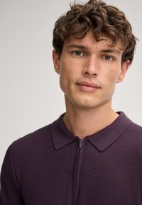Dunkelviolettes Poloshirt mit einem strukturierten Strickmuster, kurzem Reißverschluss und klassischem Kragendesign.