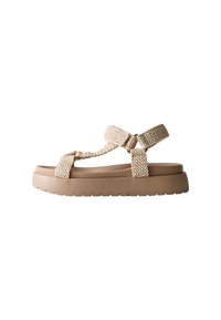 Beige plattformssandaler med texturerade vävda remmar och en platt gummisula. Har en korsad design och justerbar ankelrem för en bra passform.