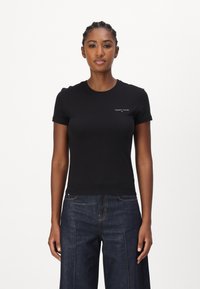 Černé bavlněné tričko s krátkými rukávy, přiléhavý střih a malé bílé logo "Tommy Jeans" na hrudi, v kombinaci s tmavými džíny.