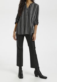 Randig blus i svart och vitt med knappslå och uppvikta ärmar, kombinerad med svarta byxor i imitationläder med utsvängda ben och ankle boots.