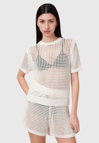 Strikket, elfenbensfarvet mesh top med korte ærmer, der har en rund udskæring og store åbne huller; parret med matchende shorts med lignende mønster.