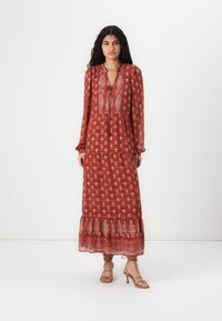Robe longue de couleur rouille avec imprimé botanique blanc, décolleté en V et détails à cordon. Présente un ourlet évasé et des manches longues froncées.