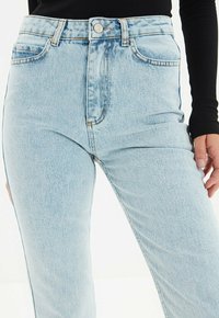 Jeans de tiro alto en azul claro, hechos de denim, con diseño de cinco bolsillos, acentos de costura vertical y cierre de botón en la cintura.