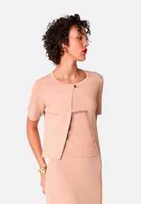 Zweiteiliges Strickoutfit in zartem Rosa, bestehend aus einem kurzärmligen Oberteil mit rundem Ausschnitt und einem dekorativen Verschluss, kombiniert mit einem figurbetonten Rock.