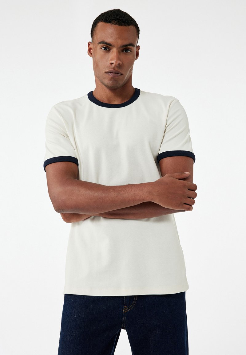 T-shirt color crema con colletto a costine blu navy e polsini, realizzato in tessuto morbido, con maniche corte e vestibilità rilassata.