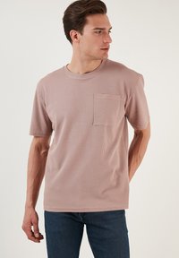 Světle růžové triko s krátkým rukávem a kapsou, vyrobené z texturované tkaniny. Klasický design s kulatým výstřihem a jednou kapsou na prsou. Standardní střih.