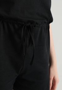 Zwarte katoen jumpsuit met een elastische tailleband met een aantrekkoord. Gladde textuur, korte mouwen en zonder opvallende patronen of accenten.