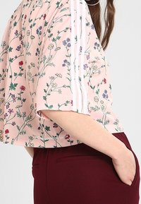 Avskuren t-shirt med rosa blommönster och gröna samt flerfärgade blommor. Har vita ränder längs ärmarna. Matchas med bordeauxfärgade byxor.