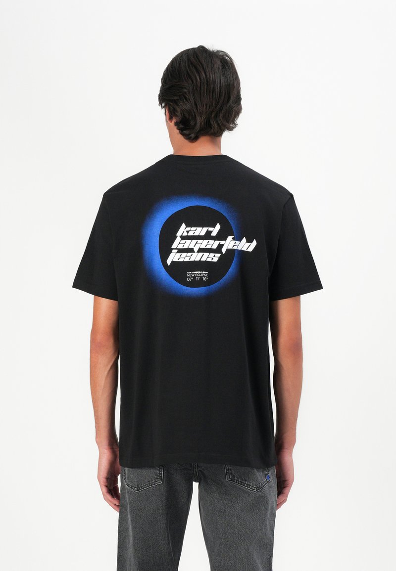 Fekete pamut póló, hátán kör alakú kék gradiens mintával. Fehér "karl lagerfeld jeans" felirat található egy fekete körben.