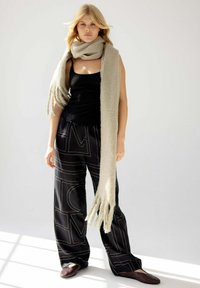 T-shirt noir, écharpe beige, pantalon noir à jambes larges avec un motif géométrique, et chaussures plates sombres. Textures douces et couleurs neutres.