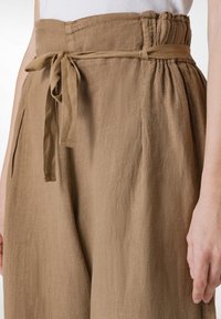 Bruna linnbyxor med hög midja, veck och knytbälte. Texturen är mjuk, med en naturlig finish och avslappnad passform.