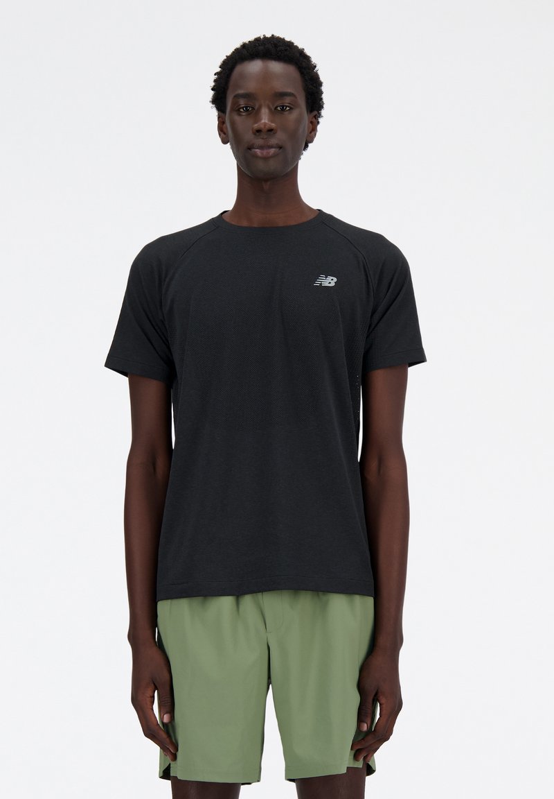 Black short-sleeve athletic shirt with mesh texture and New Balance logo, paired with green shorts. Simple, athletic fit design.